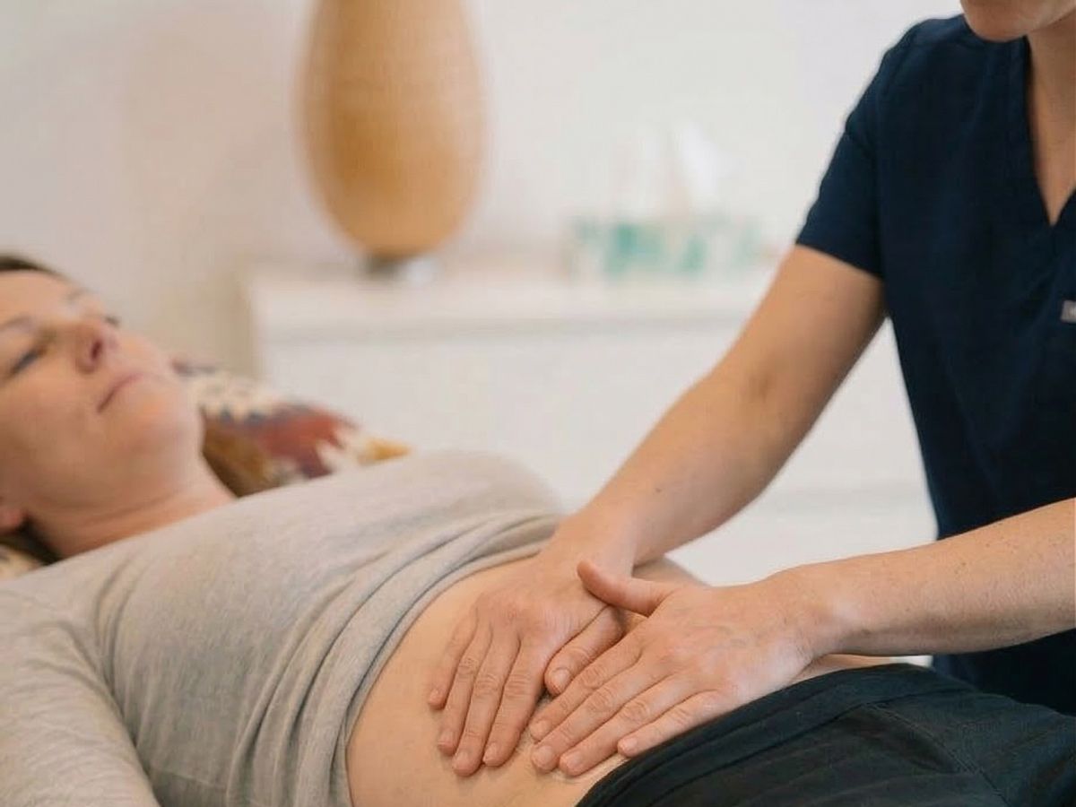 Therapeutin legt beide Hände sanft auf den Bauch einer Patientin auf der Behandlungsliege – Narbentherapie nach Kaiserschnitt in Berlin